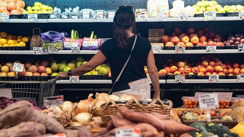 A woman looks at apples in a supermaket aisle.