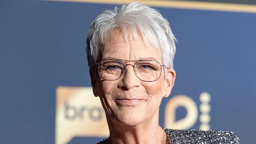 Jamie Lee Curtis smiling, it's a close-up head shot and she has short, grey hair and glasses