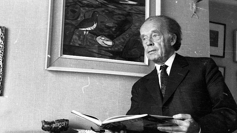 A black and white image of Childers in a suit holding a book. He has short dark hair.