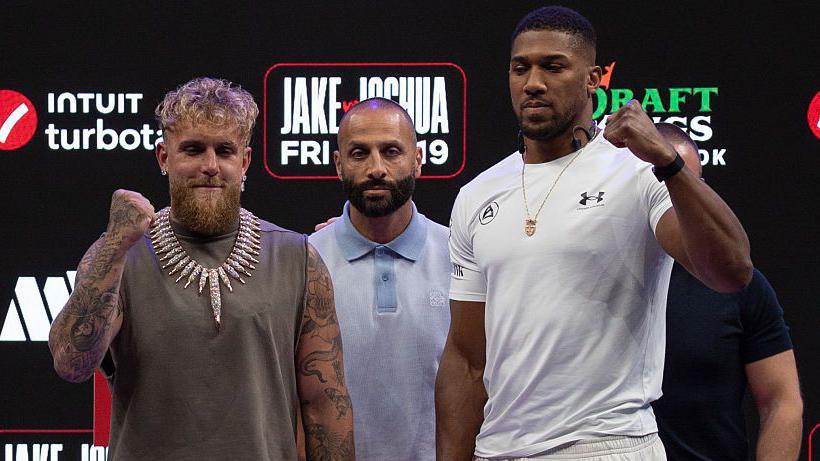 Jake Paul and Anthony Joshua hold up their fists as they pose for pictures side-by-side