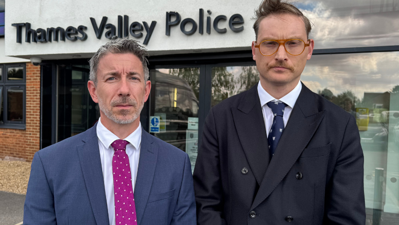 Two men in suits - one slightly shorter than the other - looking into the camera with serious facial expressions. They are stood in front of Thames Valley Police's Headquarters.