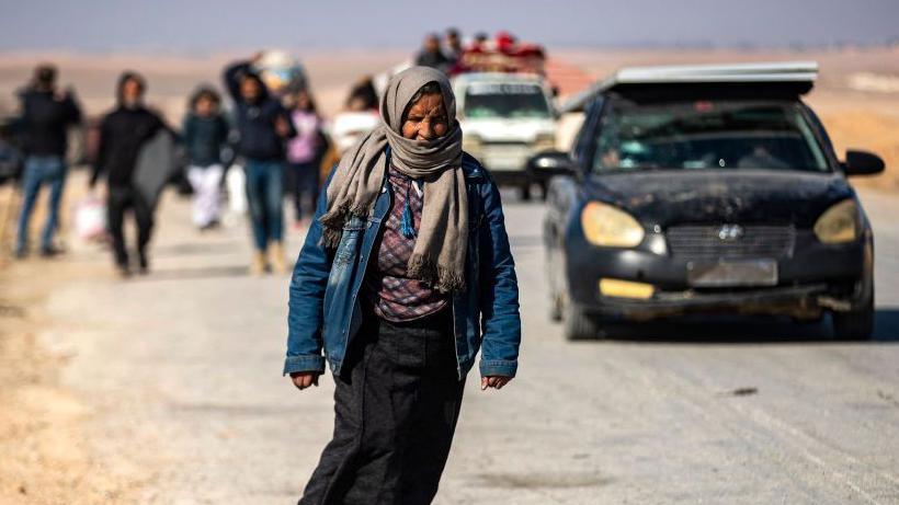 Displaced Syrian Kurds walk along the road as they flee