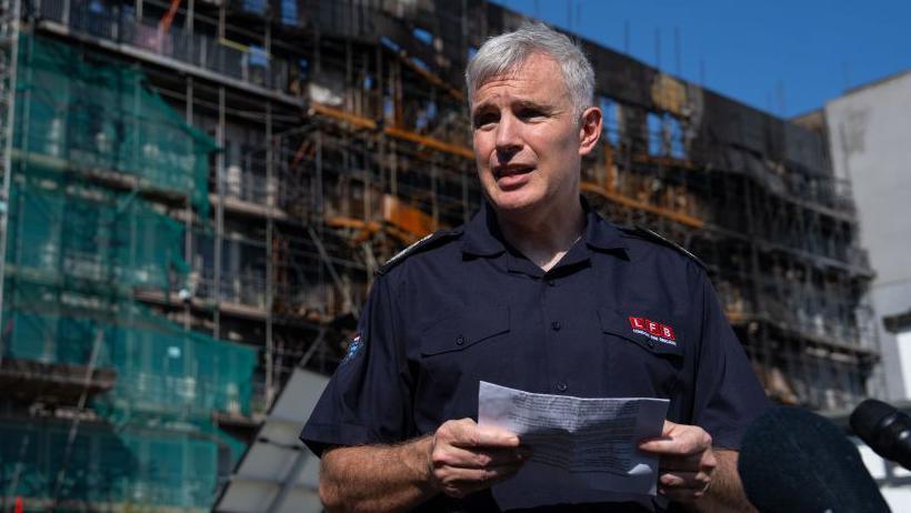 Andy Roe addresses the media outside the scene of a fire. He is holding a piece of paper. 