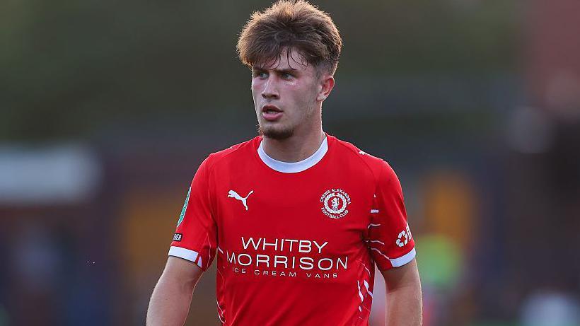 Luca Moore wearing a red Crewe Alexandra shirt looks on during a game