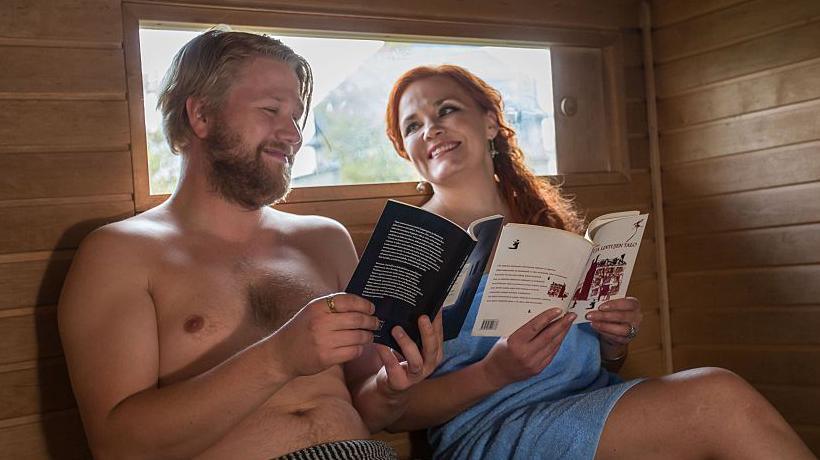 Finnish authors Harri Hertell (L) and Katariina Vuorinen, both wearing only towels, smile and hold books as they give a reading in a mobile sauna - file photo