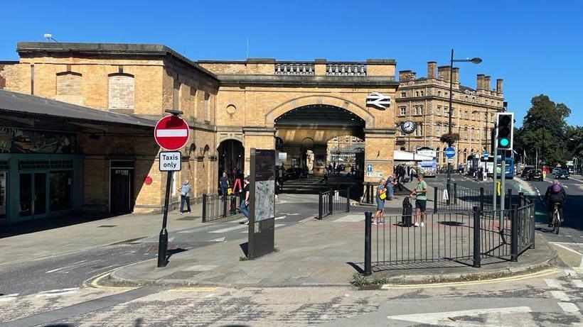 The outside of York Station, with people walking by and buses parked at the front.