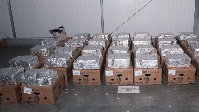 Dozens of cardboard boxes lined up on the floor of a warehouse. There are silver packages on top of every box.