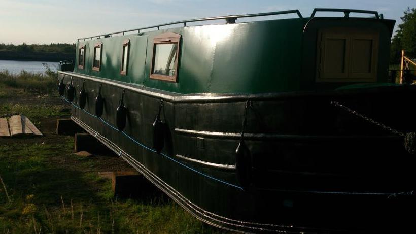 A green narrow boat facing out to the river