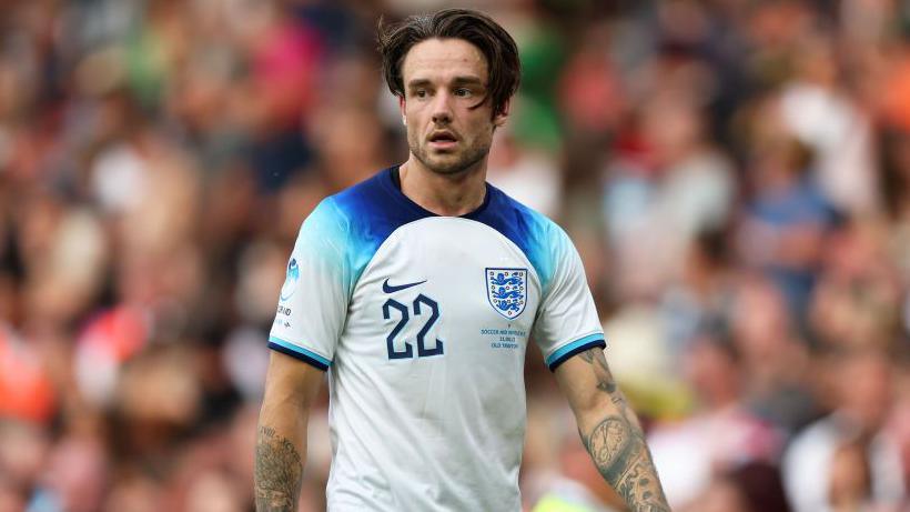 Liam Payne wearing a blue and white football t-shirt with the number 22 printed in the left corner. He has short brown hair and crowds are standing behind him