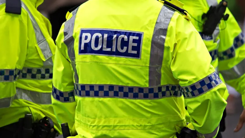Image shows the back of a police officer's florescent yellow-green jacket. It has the word POLICE written in white capital letters on a blue background.