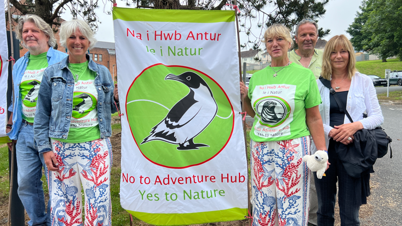 Protestwyr gan ddal baner yn nodi 'Na i Hwb Antur, Ie i natur'.