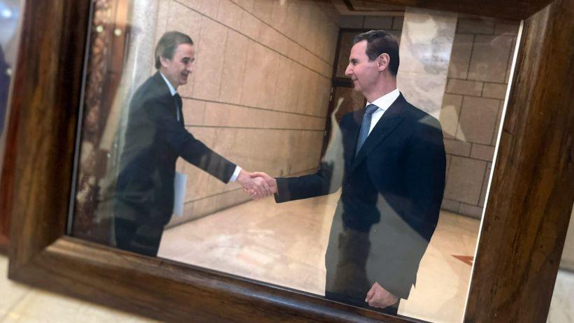 A photograph in  wooden frame shows Hassam Luka and Assad shaking hands.