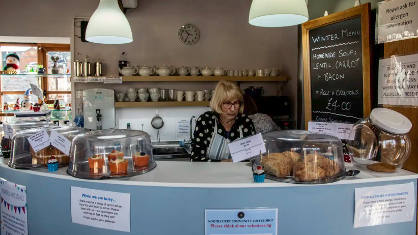 A volunteer behind the counter with piles of fresh cakes in the foreground.