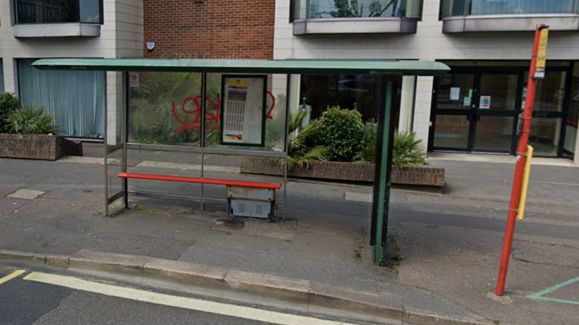 Bus stop in Bournemouth with red bench. The clear panel behind the bench has red graffiti sprayed on it.