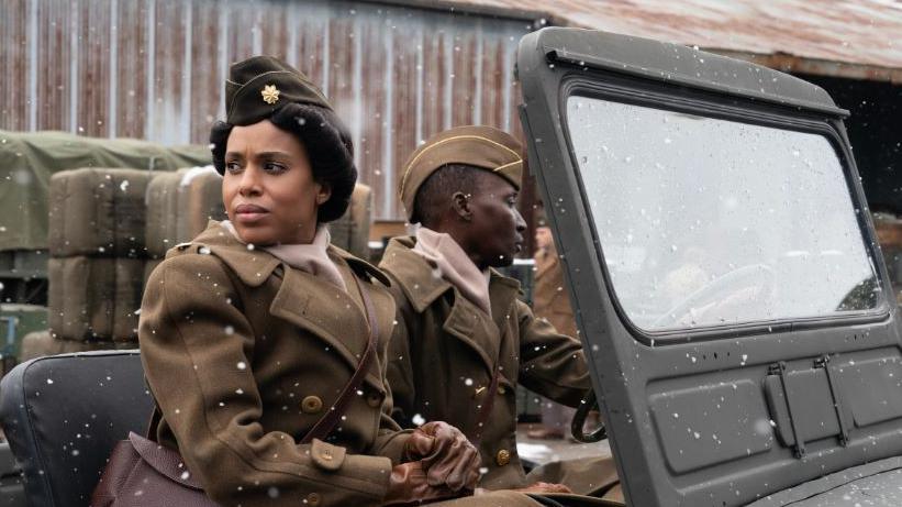 Kerry Washington playing Maj Charity Adams. She wears a US Women's Army Corps uniform, with a cap on her short, rolled back hair. She is also wearing a brown coat and looking over to her right. She is sitting in a US open top jeep, and to her left is a driver in uniform, looking the other way. he is also black.