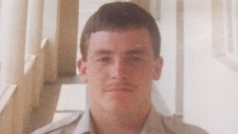 Late former soldier Stephen Kerry-Jones is looking straight at the camera. He has brown hair, in a short, military-style cut and a thin moustache. He is wearing a light-brown army shirt. The picture was taken in the late 1980s while Stephen was serving overseas with the British Army.