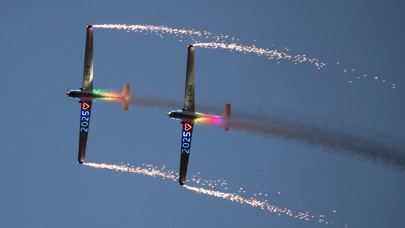 Two planes flying in-sync with one another. They have 2025 illuminated under their winds with a love heart. 