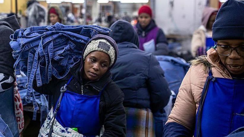 A woman, wearing a blue apron and black jersey, carries denim products in a garment factory in Lesotho