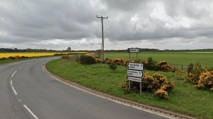 A curved road surrounded by fields with a road sign in the middle of the frame.