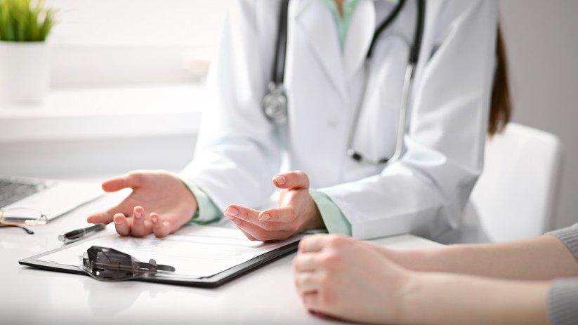 Doctor sitting with patient. Doctor has palms facing up over a clipboard