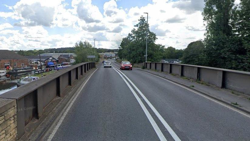 Google Maps image showing red and white cars travelling across a bridge over a canal.