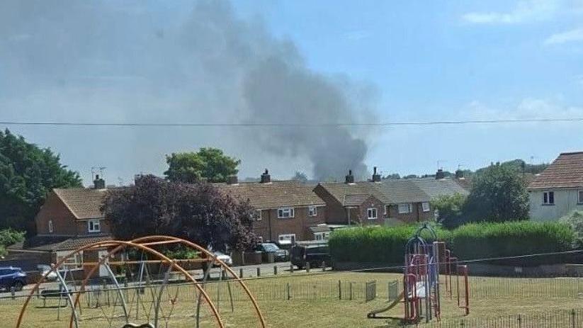 Grey smoke billowing into the sky. A playground is in the foreground of the picture.