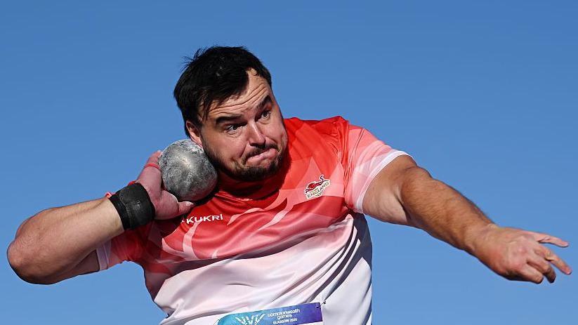 Scott Lincoln in a red and white Team England vest competing in the shot put