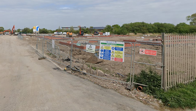 A plot of empty industrial land with fencing and signage