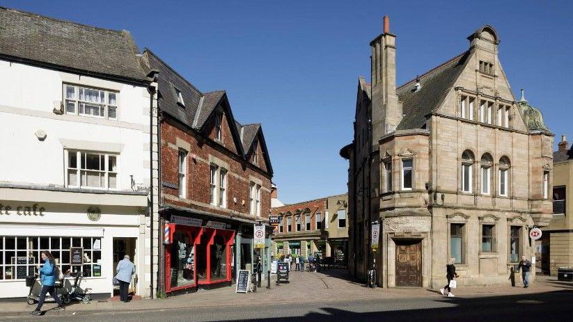 A picture of the High Street Heritage Action Zone, Priestpopple, Hexham, Northumberland. It shows a curved street and stone buildings.
