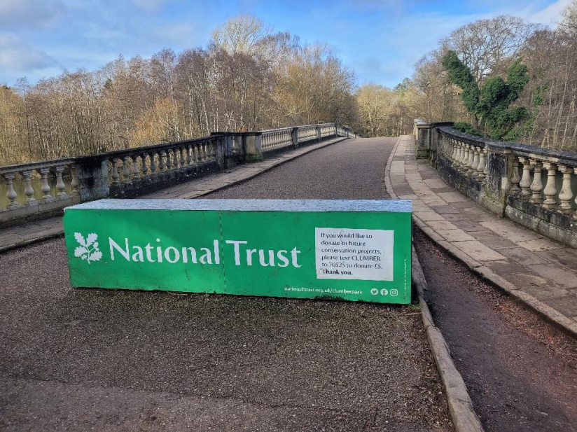 A concrete block left across the road accessing the bridge, with bold green National Trust branding