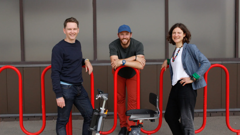 Tom, Fred and Emily, all smiling into camera, standing by railings with their 3Scooter in the foreground