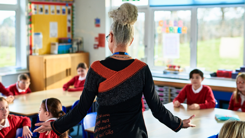 Primary school teacher standing with arms out, preparing children for class.