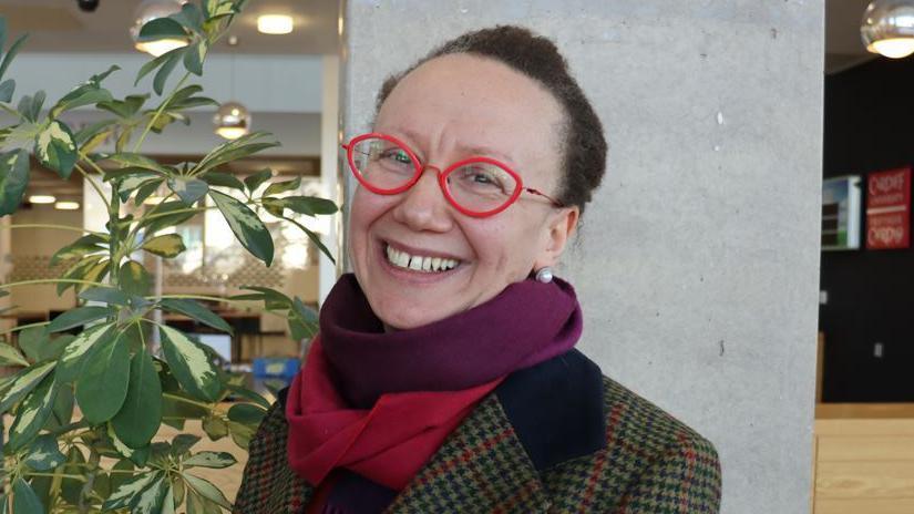 Cardiff University's Prof Arianna Di Florio smiles broadly in a pair of red-rimmed spectacles and a houndstooth pattern jacket 