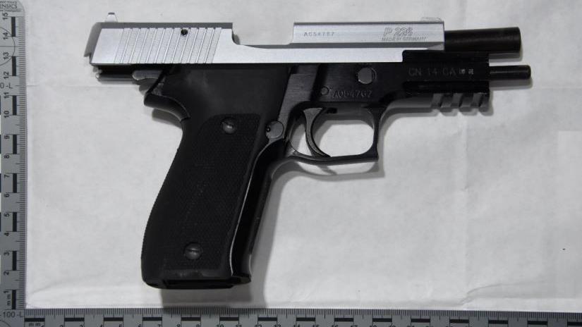 A 9mm pistol laying on a sheet of paper on a table, taken from above. The barrel has been cocked open and is empty. On either side of the gun is a measuring ruler.