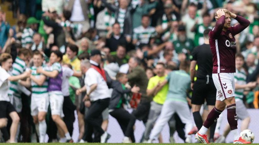 Celtic fans celebrate with their players on the pitch as Hearts' Stephen Kingsley is left stunned