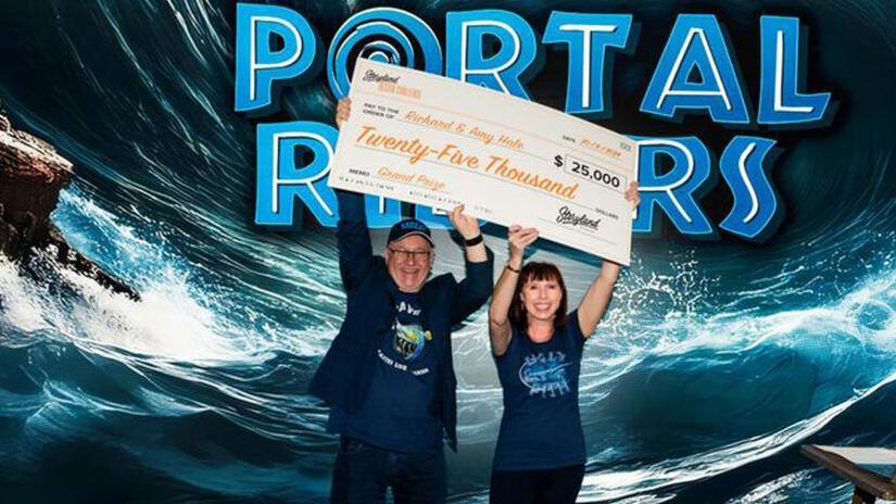 Richard and Amy Hale smiling while holding the cheque for $25,000, which they won for designing the theme park ride Portal Riders.