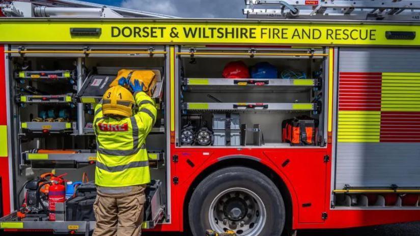 A generic picture of a firefighter packing away items into a fire engine