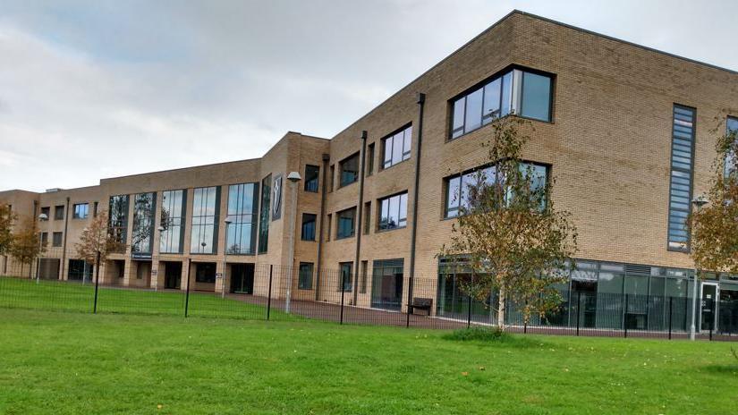 General view of caldicot school - orange brick building with trees and green grass inside a tall fence