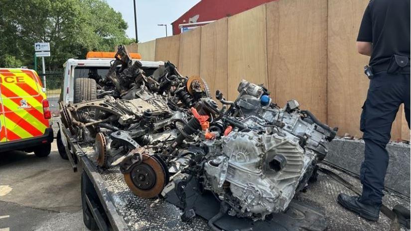Car engines were among the parts, thought to be from stolen vehicles, discovered at a 'chop shop' at a garage in Thrybergh, Rotherham. A South Yorkshire Police officer stands on the right of the flatbed truck taking the car parts away, with a police van to the left