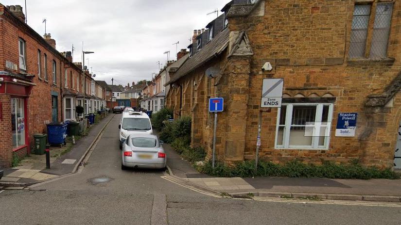 A Google street view of Newlands Place, a narrow road with houses on either side, and lined with parked cars on one side. It leads off from a main road. A Chinese takeaway is on the left, a church on the right.