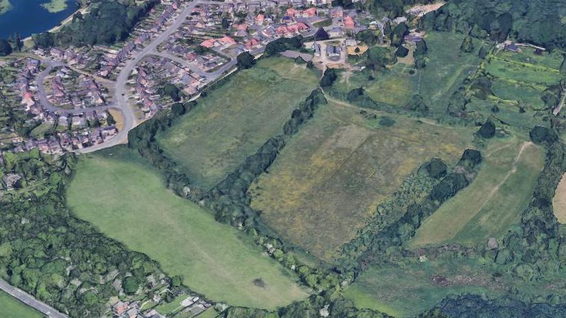 An aerial view of the proposed development site, consisting of two fields on the edge of a older housing area