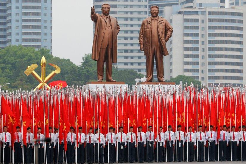 Students carrying party flags stand under statues of former North Korean leaders Kim Il Sung and Kim Jong Il