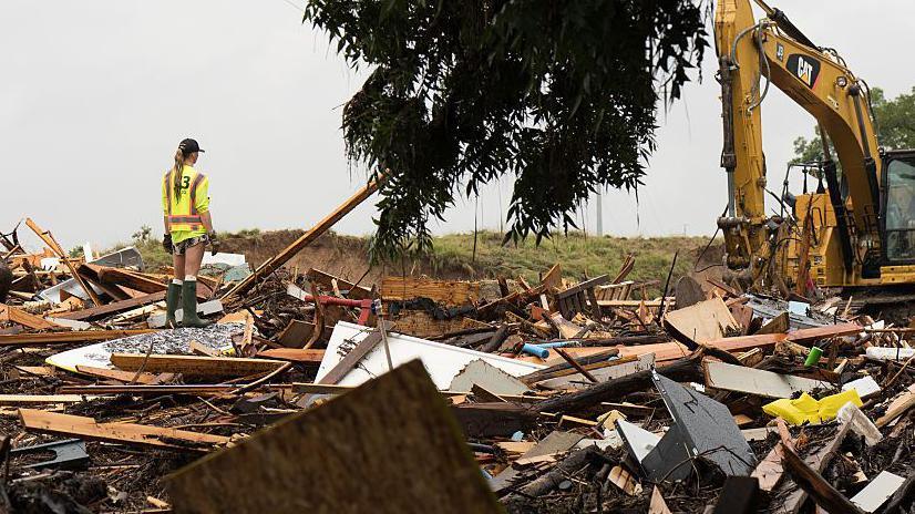 Workers operate heavy machinery to clear debris after massive flooding