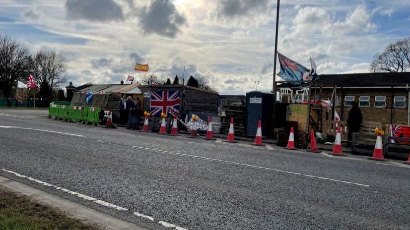 Tents, wooden huts and flags flying outside the former RAF Scampton's main gate