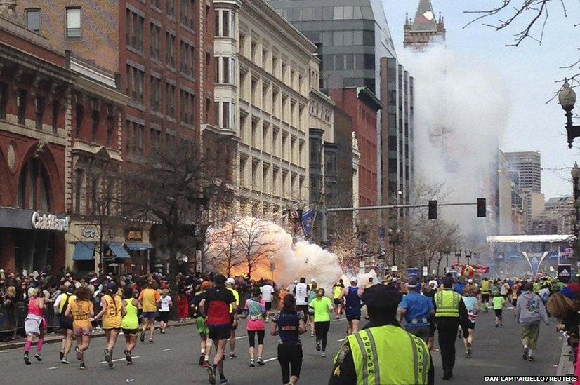 Runners continue to run towards the finish line of the Boston Marathon as an explosion erupts near the finish line of the race