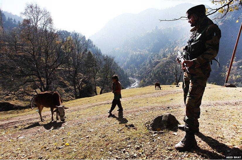 A Kashmiri Muslim girl walks as an Indian army soldier stands guard near the Line of Control with mountains of Pakistani side of Kashmir in the background, in Uri, some 125 km north of Srinagar