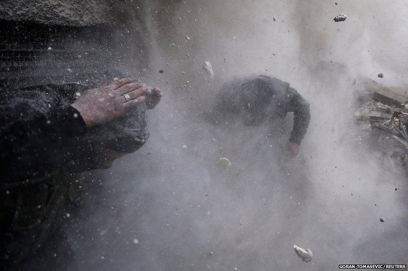 Syrian rebel fighters taking cover amid flying debris and shrapnel after being hit by a tank shell in the Ain Tarma area of Damascus