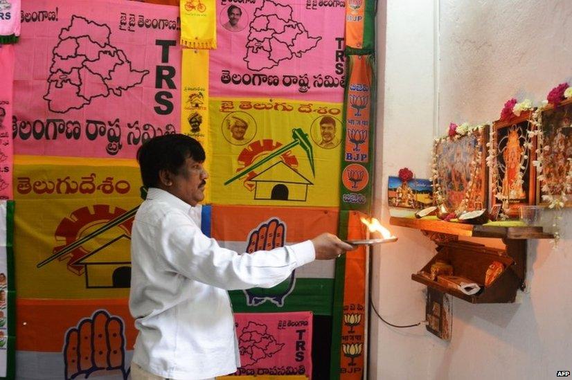 An Indian man offers prayers as he stands in front of different party campaign flags displayed at his workshop in Hyderabad.