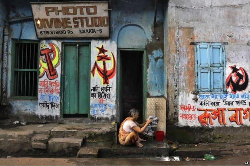 An elderly Indian woman washes clothes on her doorstep beside election graffiti of the Communist Party of India (Marxist) in Kolkata