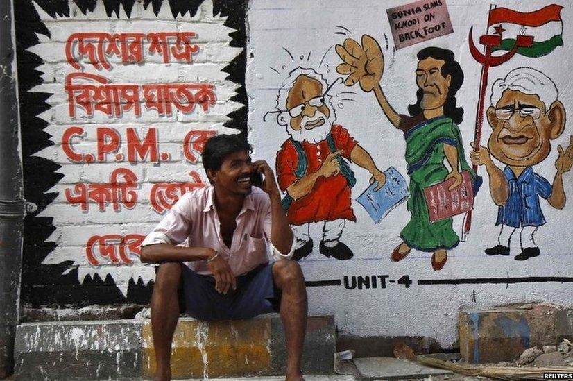 A man speaks on his mobile phone in front of graffiti depicting Indian political figures on a wall ahead of the general election in Calcutta.